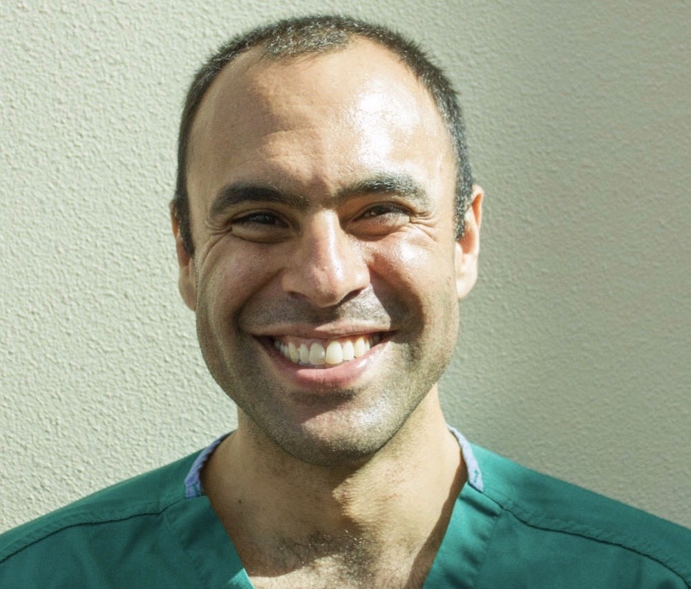 Ben Mati smiling in green scrubs against a light wall