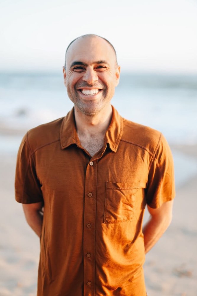 Ben Mati smiling on a beach in an orange shirt