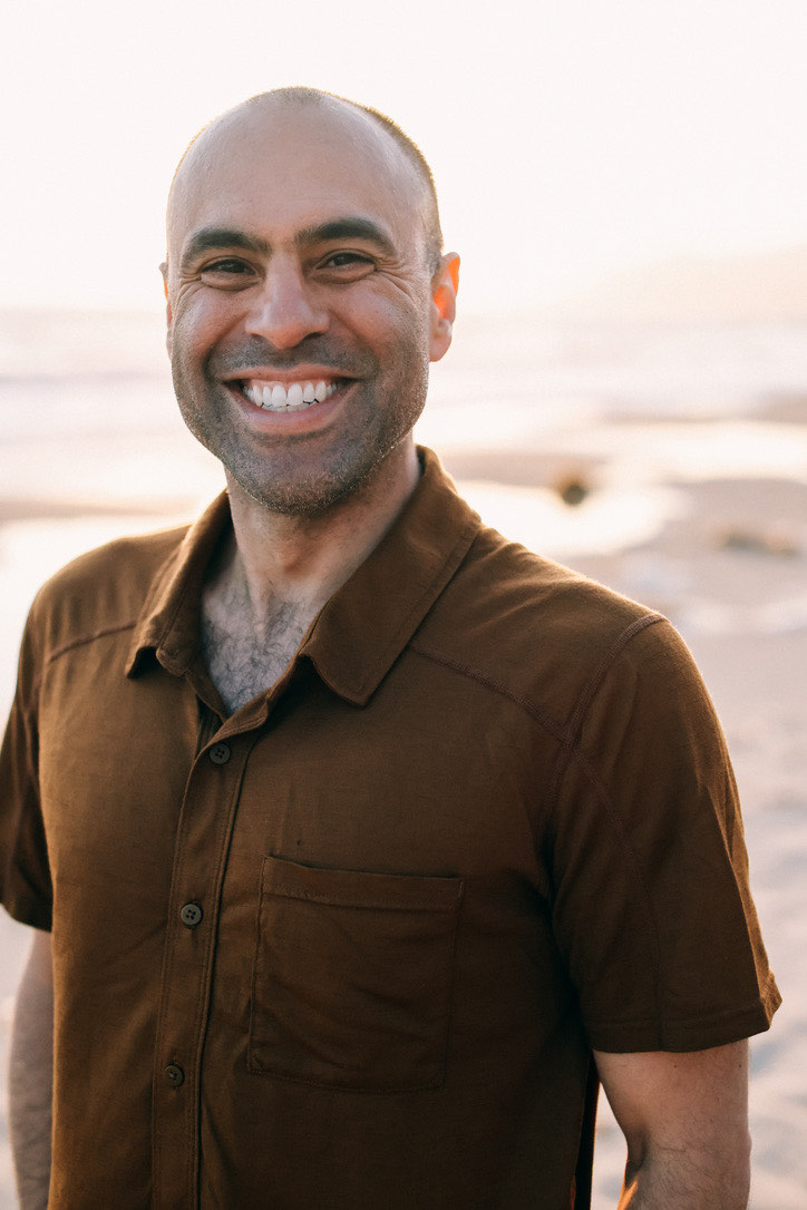 Ben Mati smiling on the beach at golden hour in a brown shirt